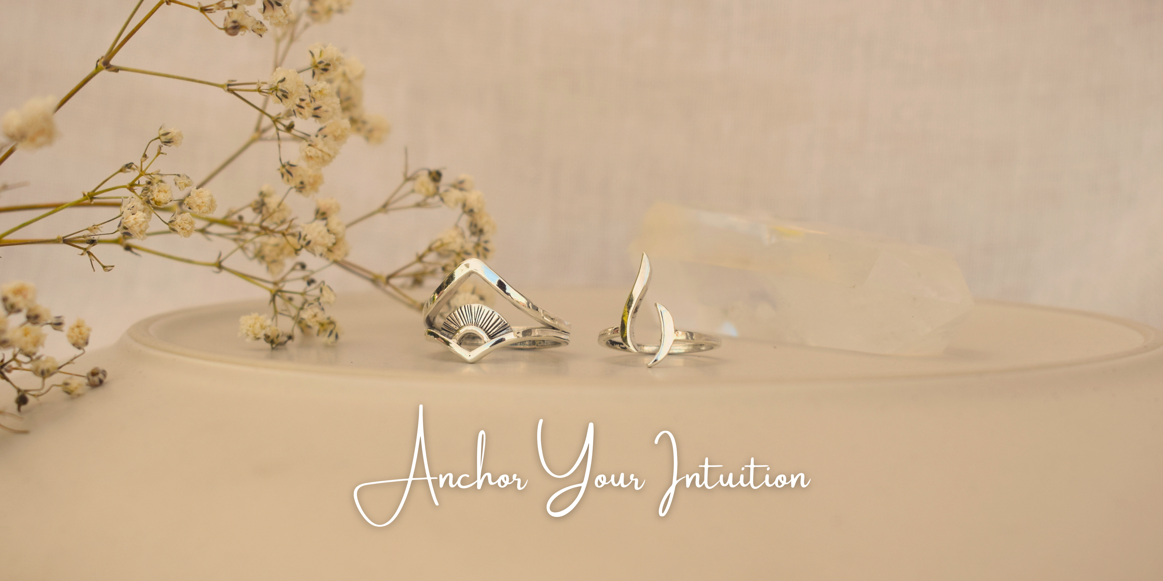 Silver rings on a beige surface with dried flowers, text 'Anchor Your Intuition' on a beige background