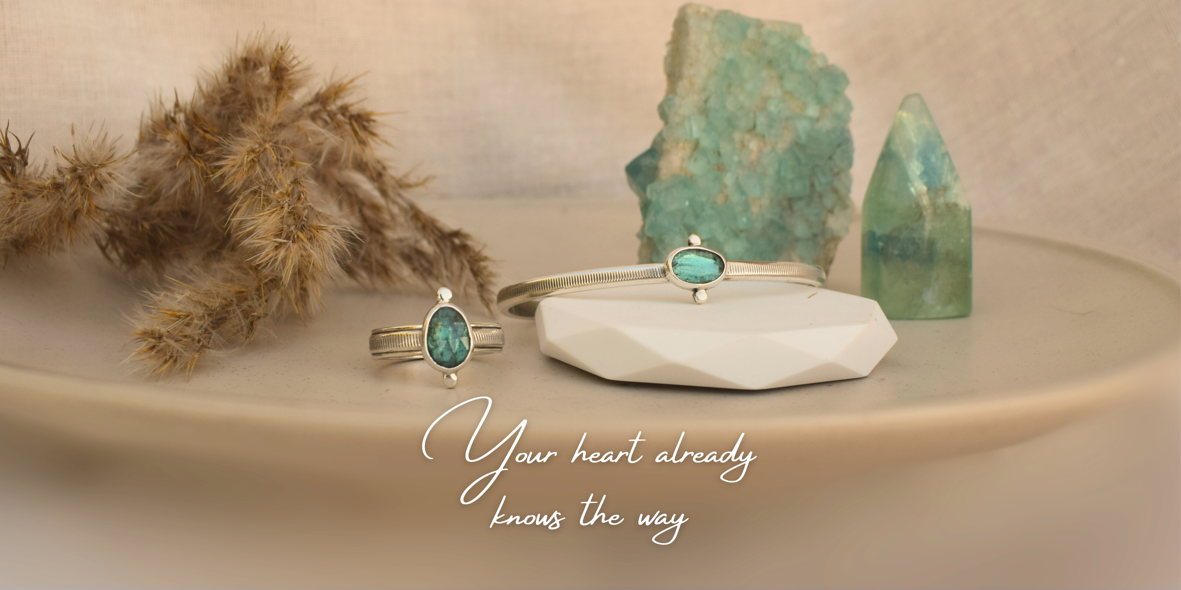 Jewelry set with emerald stones on a neutral background with text 'Your heart already knows the way'.
