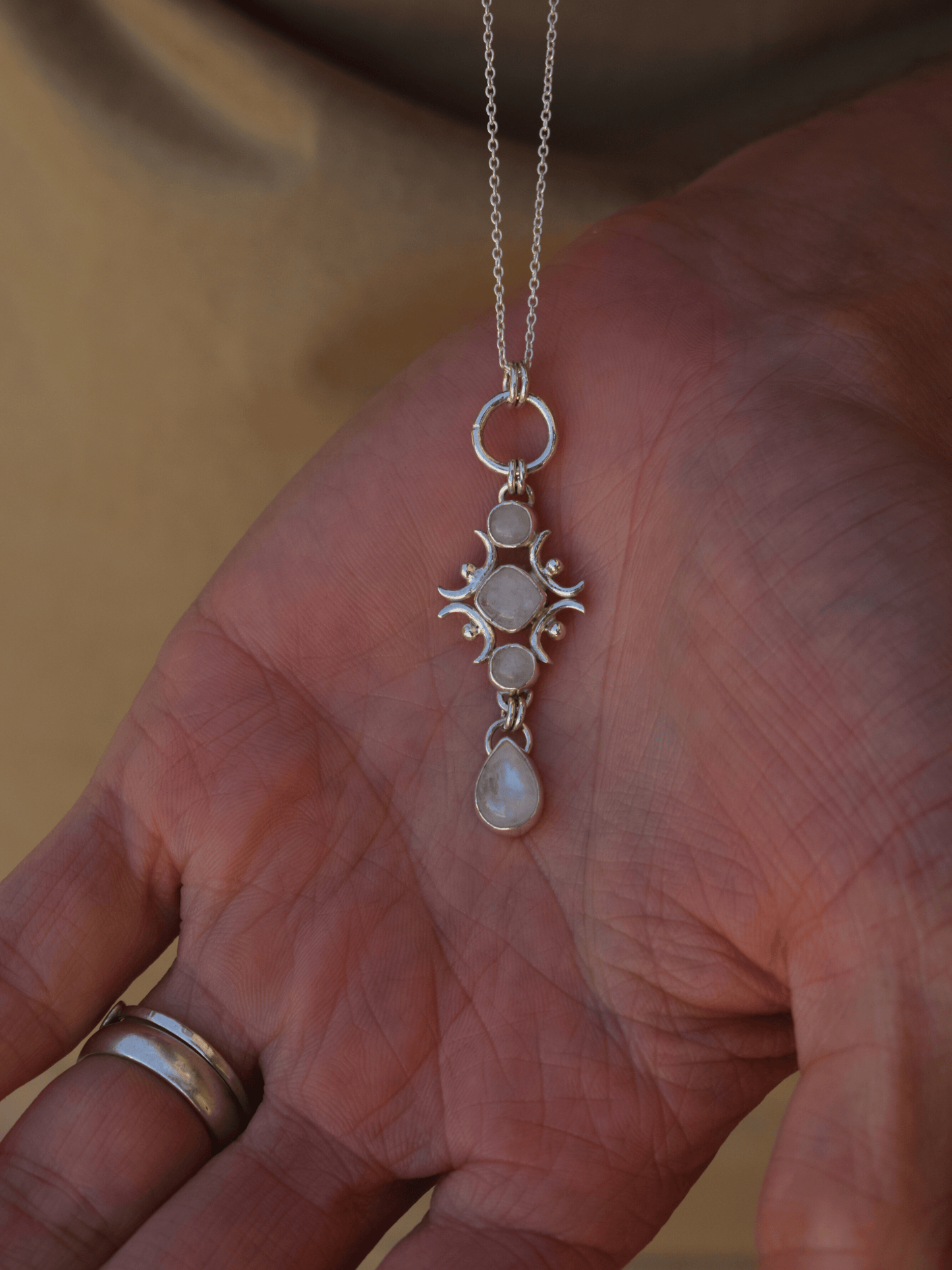 silver moonstone necklace hanging over hand with silver ring